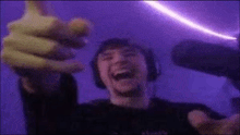 a man wearing headphones is laughing and holding a microphone in front of a purple light .