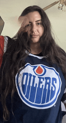 a woman wearing a blue oilers jersey stands in front of a ceiling fan