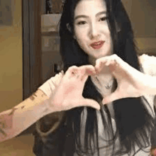 a woman with long black hair is making a heart shape with her hands .