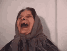 a woman wearing a scarf around her head is laughing with her mouth open .