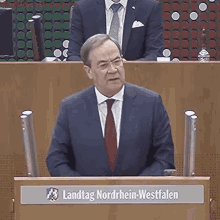 a man in a suit and tie is giving a speech in front of a podium that says landtag nordrhein-westfalen