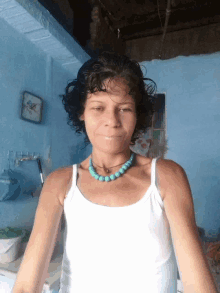 a woman wearing a white tank top and a blue necklace smiles for the camera