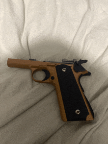 a brown gun with black grips is laying on a bed