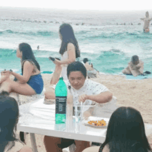 a man sits at a table on the beach with a bottle of sprite