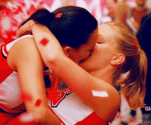 two cheerleaders are kissing in front of a sign that says gl