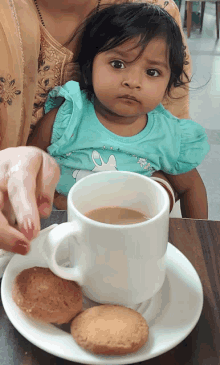 a little girl sits next to a cup of coffee and cookies