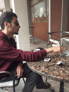 a man wearing sunglasses sits at a table with an ashtray