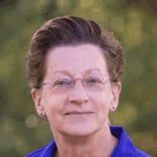 a woman wearing glasses and a blue shirt is smiling for a picture .