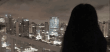 a woman is looking at a city skyline at night