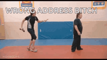 a man and a woman are standing next to each other in a gym with the words wrong address bitch above them .