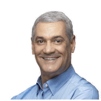 a man with gray hair and a blue shirt smiles with his arms crossed