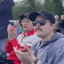 two men wearing hats and sunglasses are clapping their hands in a crowd with a caption that says tank 0 0