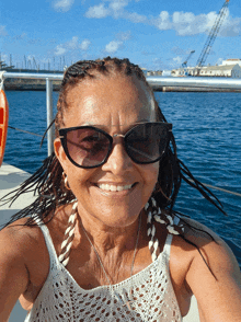 a woman wearing sunglasses and a white top smiles in front of the ocean