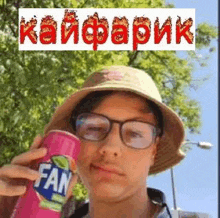 a young man wearing a hat and glasses is holding a pink fanta can .