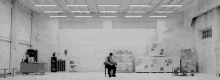 a black and white photo of a man sitting in a chair in a warehouse