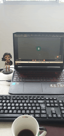 a cup of coffee sits on a desk next to a laptop with the letter b on the screen