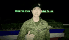 a young man in an army uniform salutes in front of a sign that says serving the people securing the land .