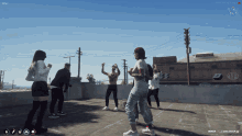 a group of people are dancing on a rooftop in front of a building with a b on it