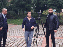 a man with a camera on a tripod stands between two men