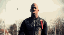 a bald man in a black jacket is holding a red object