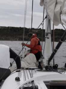 a man in a red jacket is holding a sail on a boat