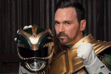 a man in a green ranger costume holds a helmet