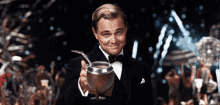 a man in a tuxedo is holding a glass with a straw in it