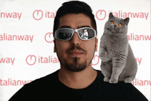 a man wearing sunglasses holds a cat on his shoulder in front of a sign that says italianway