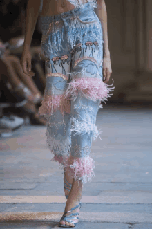 a model walks the runway at a fashion show wearing a pair of jeans with flamingos embroidered on them