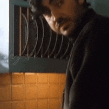 a man with a beard is standing in a kitchen in front of a shelf with plates on it .