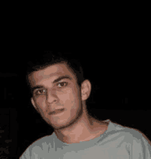 a young man in a grey shirt is looking at the camera in the dark .