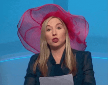 a woman wearing a large red hat holds a piece of paper