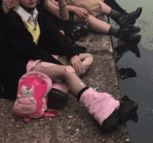 a girl wearing a pink hello kitty backpack sits on the ground