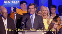 a man in a suit and tie is giving a speech in front of a crowd with a kentucky sign behind him .