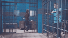 a man in a blue shirt is standing in a jail cell talking to a woman