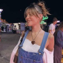 a woman wearing overalls and a necklace stands in front of a sign that says " ice cream here "