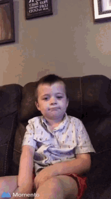 a young boy is sitting on a couch with a sign on the wall that says " a child is a gift from god "