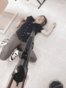 a woman is laying on the floor with a gun pointing to her .