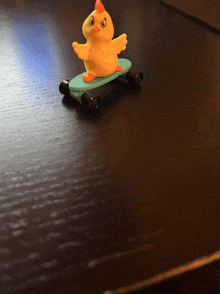 a toy chicken on a blue skateboard on a table