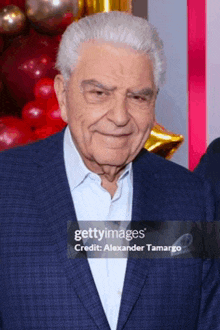 an older man in a suit and blue shirt is smiling for the camera .