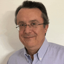 a man wearing glasses and a light blue shirt smiles for the camera