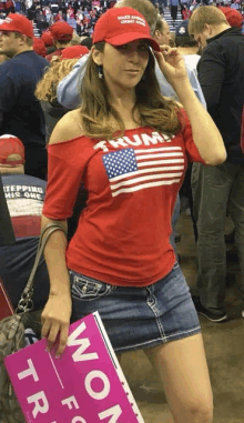 a woman wearing a red shirt that says trump holds a sign that says women for trump