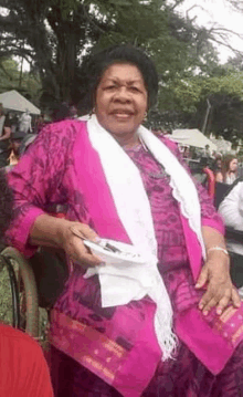 a woman in a pink dress and white scarf is holding a plate of food in her hand .