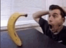 a man is sitting at a table with his mouth open in front of a large banana .