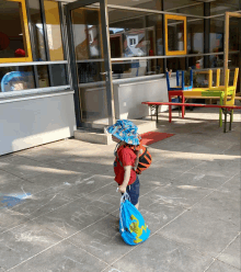 a young boy wearing a blue hat and carrying a blue backpack with a map of the world on it