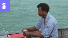 a man sits on a boat with a cooler in front of him with the letter s in the background