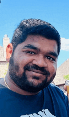 a man with a beard wearing a blue adidas shirt smiles for the camera