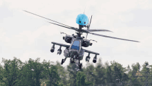 a military helicopter flying over a forest with a blue object on top of it