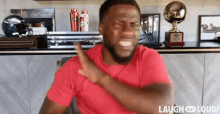 a man in a red shirt is making a funny face while sitting in front of a table with trophies .