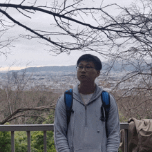 a man wearing glasses and a backpack is standing in front of a city